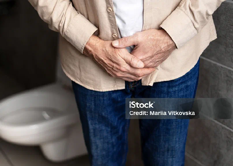 A man standing in a bathroom with his hands clasped at his waist
