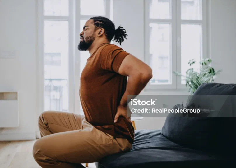 A man sitting on a bed holding his lower back