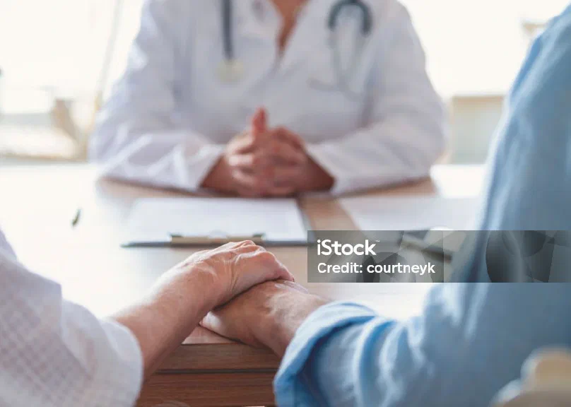 A couple holding hands across a desk from a doctor