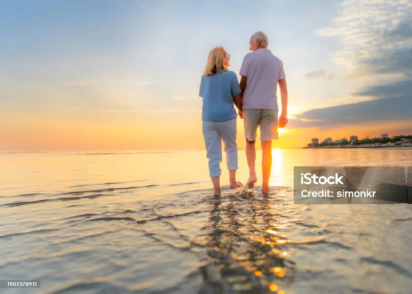 A couple walking hand in hand along a beach at sunset