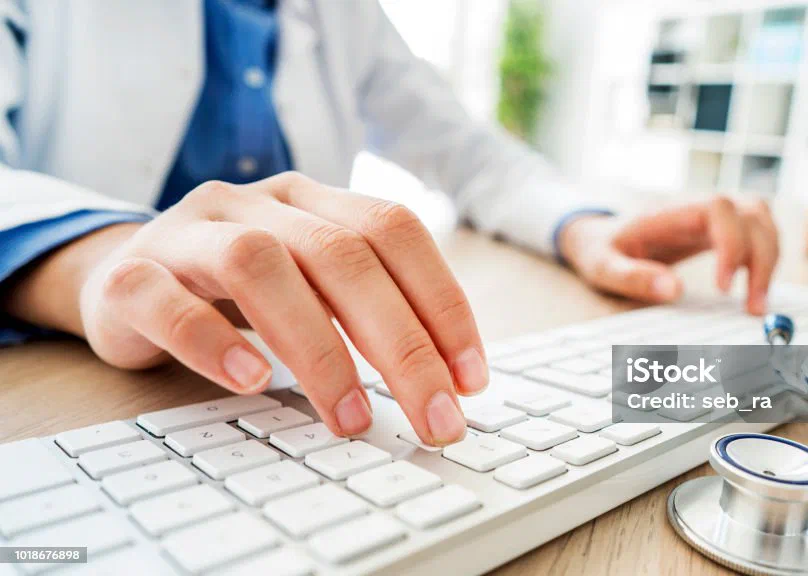 Hands typing on a keyboard beside a stethoscope