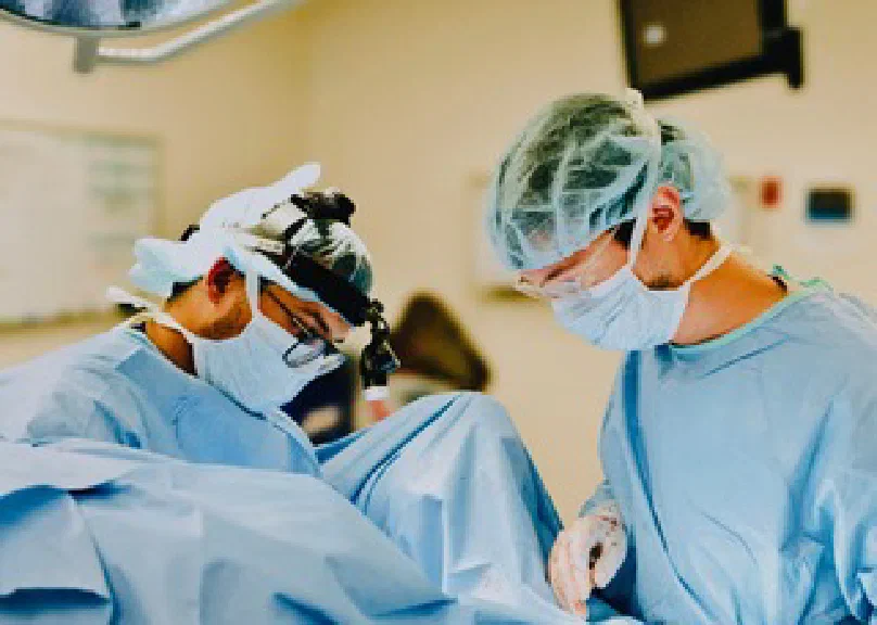 Two surgeons in scrubs and loupes working in an operating room
